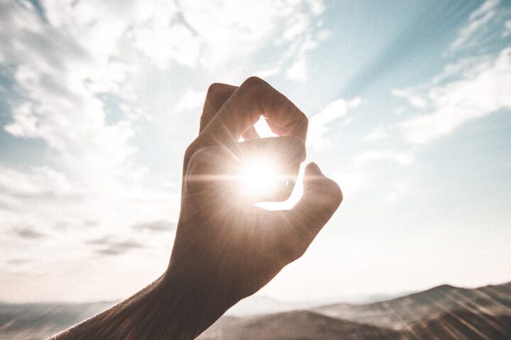 photography of sun glaring through the hole of finger